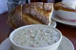 Bowl of creamy clam chowder served with a slice of crusty bread, featured in ExploreTraveler's 'Eat Like A King' series, highlighting culinary delights.