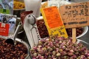 Colorful spices and dried rose buds in market display, featuring labels in Hebrew, highlighting culinary experiences related to food in Israel, particularly near the Church of the Annunciation in Nazareth.