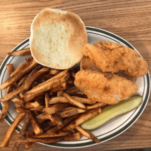 Fried chicken with crispy fries, a toasted bun, and a pickle slice on a plate, representing a culinary experience related to fried chicken.