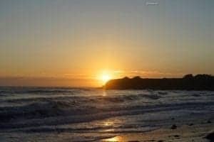 Misty sunset over Big Sur Beach, California, with waves gently lapping at the shore and cliffs silhouetted against the vibrant sky.