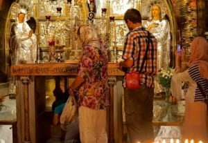 Visitors at the Church of the Holy Sepulcher, observing the altar adorned with silver decorations and religious icons, highlighting its significance as a historical and spiritual travel destination.