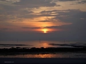 Malaysian beach sunset view over calm waters, showcasing vibrant orange and purple hues in the sky, reflecting on the surface, highlighting the tranquil beauty of Malaysia's coastal scenery.