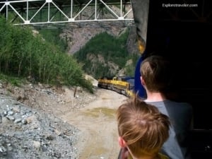 Children observing the Alaska Railroad train traveling through a scenic landscape near Denali, highlighting the experience of train travel on the Denali Star route.