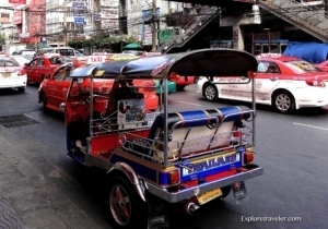Tuk-tuk vehicle in busy Bangkok street, showcasing local transportation amidst red taxis, highlighting travel experience in Thailand.