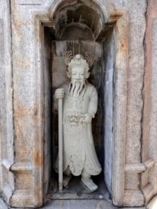 Chinese stone guardian statue at the Temple of Dawn (Wat Arun) in Bangkok, Thailand, featuring intricate details and a traditional stance with a staff.