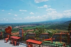 Lush green valleys of Majalengka, Indonesia, viewed from Paraland, featuring red outdoor seating and scenic mountainous backdrop.
