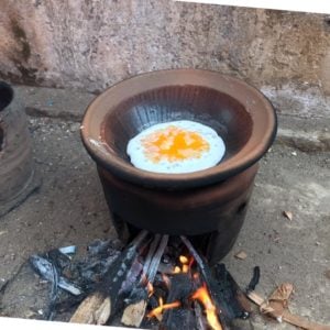 Traditional Sundanese cake Serabi cooking in a clay pot over an open flame, featuring a layer of coconut batter topped with egg yolk.