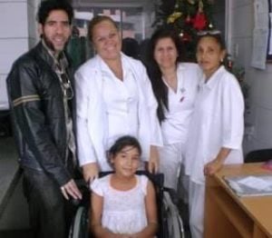 Group of healthcare professionals and a young girl in a wheelchair, smiling together in a hospital setting, reflecting community support and care.