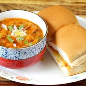 Pav Bhaji served in a bowl with chopped onions and cilantro, accompanied by soft bread rolls on a plate, showcasing the popular Indian dish.