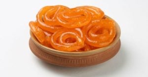 Bowl of bright orange Jalebi, a popular Indian sweet, showcasing its spiral shape and glossy texture, highlighting cultural significance in Indian cuisine.