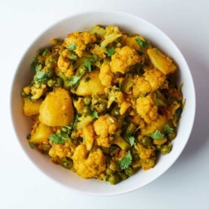 Bowl of Aloo Gobi, a popular Indian dish made with cauliflower, potatoes, and peas, garnished with fresh cilantro, showcasing vibrant yellow spices.