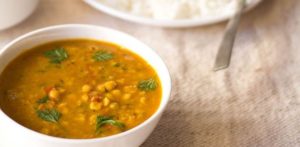 Bowl of Chana Dal soup garnished with herbs, served alongside a plate of rice, highlighting a traditional Indian dish.
