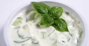 Mint cucumber raita in a white bowl, featuring diced cucumbers and a fresh mint leaf garnish, highlighting a popular Indian dish.