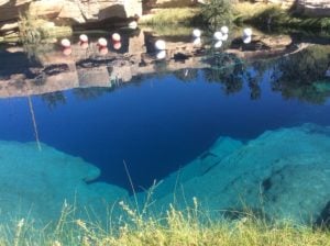 Blue Hole in New Mexico, featuring crystal-clear blue water, rocky surroundings, and floating buoys, ideal for backpacking and outdoor activities.