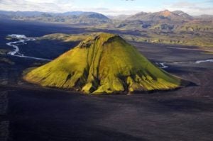 Maelifell Volcano in Iceland, featuring a lush green summit and surrounding black volcanic landscape, with distant mountains and a river visible.