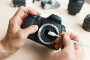 Person cleaning a camera sensor with a brush, surrounded by camera lenses, emphasizing equipment maintenance for backpacking in Iceland.