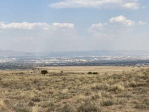 Scenic view from Albuquerque Overlook at Petroglyph National Monument, showcasing expansive desert landscape and distant mountains under a cloudy sky.