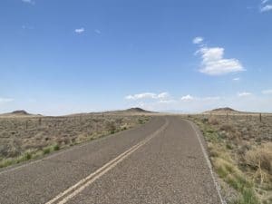 Road leading to the Three Sisters Volcanoes Petroglyph National Monument, surrounded by arid landscape and blue sky.
