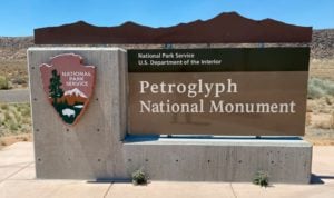 Signage at the entrance of Albuquerque's Petroglyph National Monument, featuring the National Park Service logo and text highlighting the monument's name and significance as a travel destination.