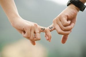 Hands of a couple with matching anchor tattoos, interlocking fingers, symbolizing connection and shared experiences in travel.
