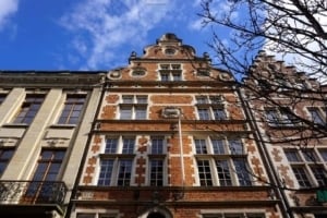 Facade of a historic Belgian building featuring intricate brickwork and architectural details, set against a blue sky with scattered clouds, showcasing the charm of Belgium's architecture.