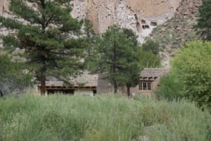 Bandelier Visitor Center surrounded by lush greenery and pine trees, with cliff formations in the background, highlighting outdoor exploration at Bandelier National Monument.