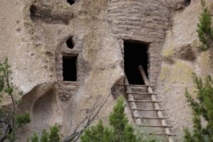 Cliffside dwelling at Bandelier National Monument with visible entrance, wooden ladder, and surrounding vegetation.