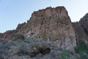 Large rock formation towering above Bandelier National Monument with visible cliffside textures and desert vegetation in the foreground, highlighting hiking scenery and natural beauty.