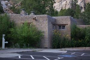 Visitor center building at Bandelier National Monument surrounded by greenery, featuring stone architecture and nearby parking area.