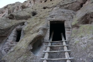 Peublo Home entrance at Bandelier National Monument with wooden ladder and rock formations, highlighting historical significance and cultural heritage.