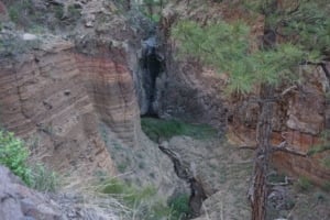 Scenic view of the Water Fall area along the Falls Trail in Bandelier National Monument, featuring cliffs, a waterfall, and lush greenery.