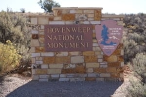 Hovenweep National Monument sign made of stone with National Park Service emblem, surrounded by desert landscape.