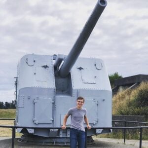 Person standing beside a historic artillery piece at Ft. Stevens State Park, highlighting the site's military history and significance.