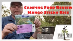 Man holding camping food package for Mango Sticky Rice, with cooking pot and outdoor setting, featuring ExploreTraveler branding and text overlay for food review.