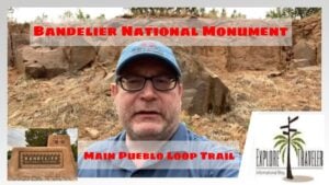 Person standing in front of Bandelier National Monument sign, showcasing the Main Pueblo Loop Trail, with ExploreTraveler logo in the corner, emphasizing backpacking destinations in New Mexico.