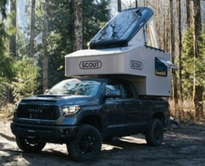 Toyota truck with SCOUT camper shell parked in a forest setting, highlighting outdoor travel trends in the USA for 2023.