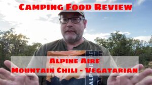 Man reviewing Alpine Aire Mountain Chili vegetarian camping food, with "Camping Food Review" text overlay, outdoor setting.