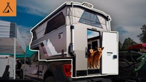 Truck camper with two dogs at the entrance, showcasing modern camping trends and outdoor lifestyle.