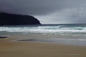 Oregon Coast beach scene with rolling waves, sandy shore, and dark, cloudy skies, highlighting the region's scenic beauty for travelers.
