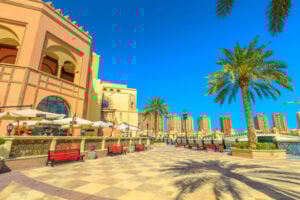 Scenic view of The Pearl-Qatar featuring palm trees, outdoor seating, and luxurious architecture under a clear blue sky, highlighting attractions for tourists in Doha.