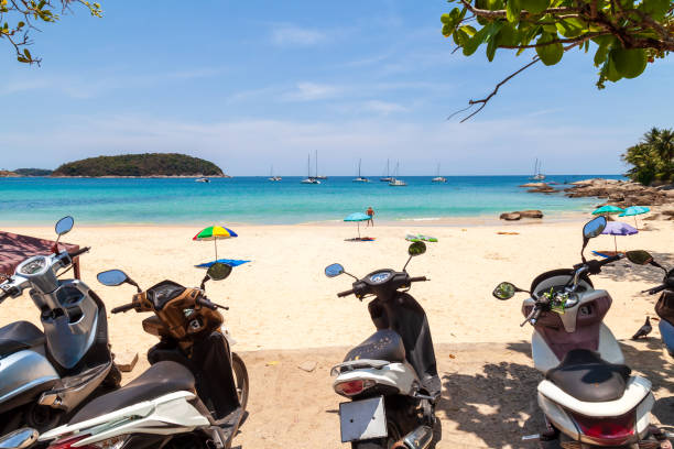 phuket island with clear turquoise water in the sea, white sand, blue sky and motorbikes for rent. 