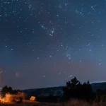 a person sitting by a campfire under a star-filled sky, surrounded by nature and feeling a sense of peace and freedom.