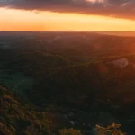 a person sitting on the edge of a cliff overlooking a beautiful sunset while surrounded by nature.