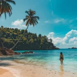 a person standing in front of a laptop on a tropical beach, surrounded by palm trees and turquoise water, showcasing the ideal digital nomad lifestyle.