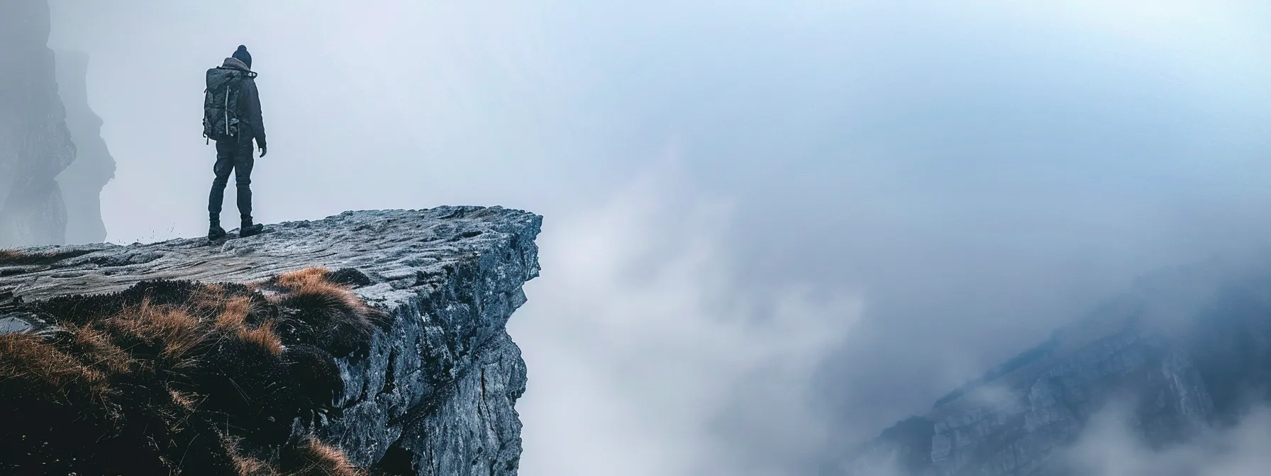 a rugged backpacker standing at the edge of a misty cliff, gazing out towards distant, uncharted lands full of promise and adventure.