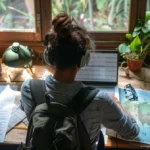 a digital nomad sitting at a laptop surrounded by travel photos, maps, and documents, looking at a spreadsheet comparing health insurance options.