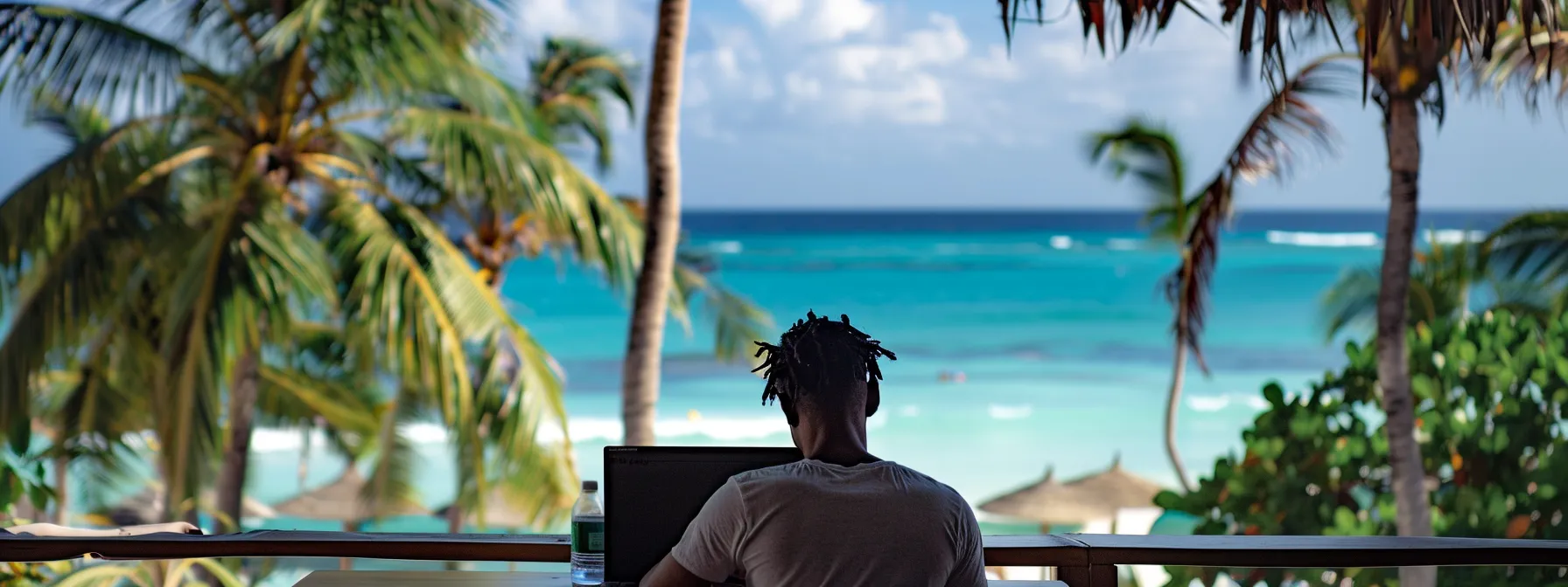 a global nomad working on a laptop with a stunning view of the turquoise caribbean sea and palm trees in the background.