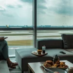 a woman enjoying a luxurious airport lounge with plush seating, a gourmet spread, and a panoramic view of the runway, despite not having a first-class ticket.